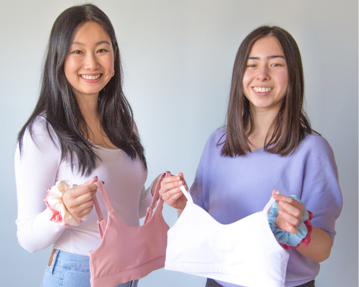 Two women holding bras in front of a white background.