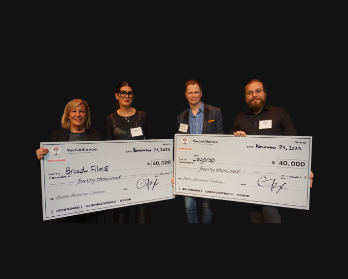 Four people holding large cheques in front of a black background.