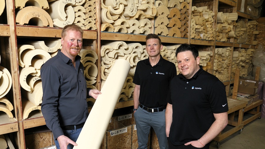 A group of people in black tshirts standing in a warehouse with wooden logs.